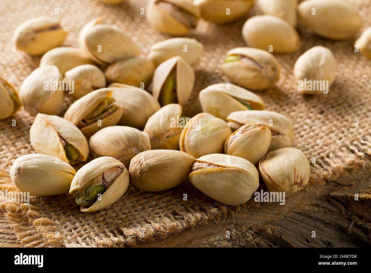 Heap of salted, roasted green pistachio nuts snack on burlap sack background, healthy food snack, selective focus Stock Photo