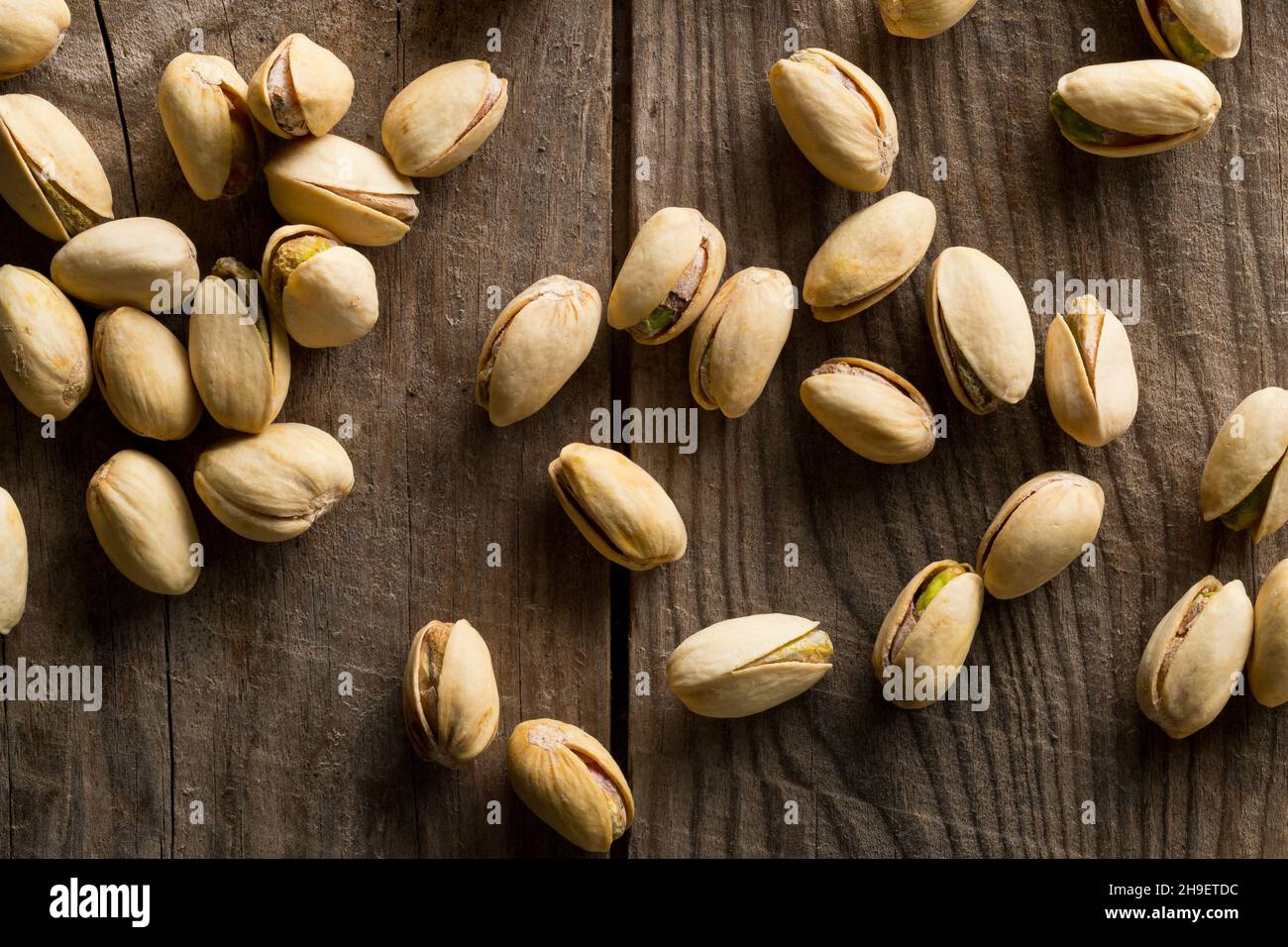 Heap of salted, roasted green pistachio nuts snack on wood background, healthy food snack, selective focus, flat lay top view from above Stock Photo