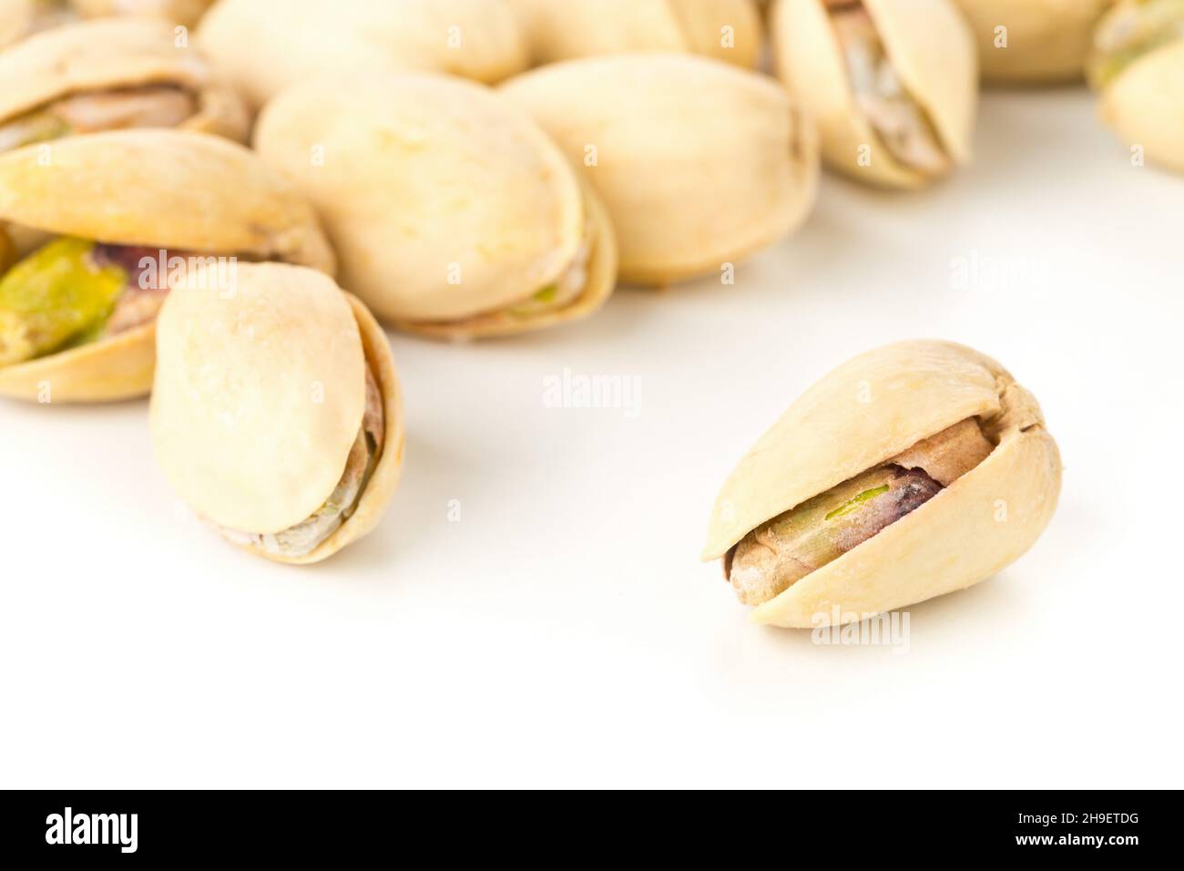 Close up of single pistachio in front of heap of salted, roasted green pistachio nuts snack over white background, healthy food snack, selective focus Stock Photo