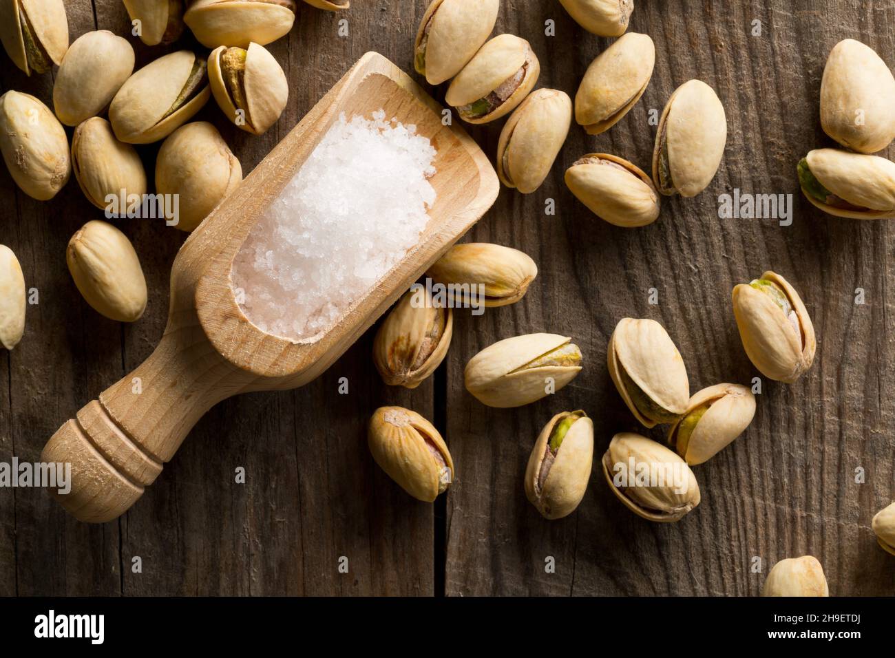 Heap of salted, roasted green pistachio nuts snack on wood background with sea salt in wooden scoop, healthy food snack, selective focus, flat lay top Stock Photo