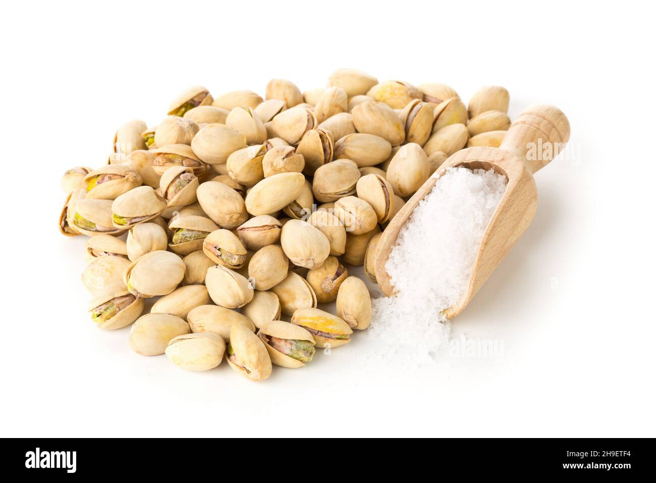 Heap of salted, roasted green pistachio nuts snack over white background with sea salt in wooden scoop, healthy food snack, selective focus Stock Photo