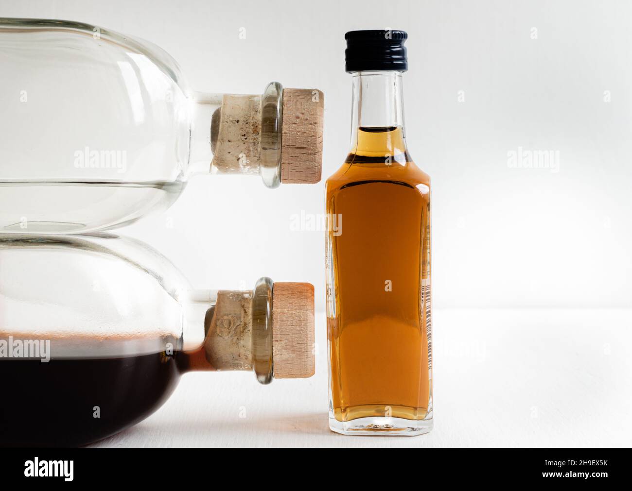 Two large glass bottles with liquids and corks vs one small with cognac on light blurred background Stock Photo