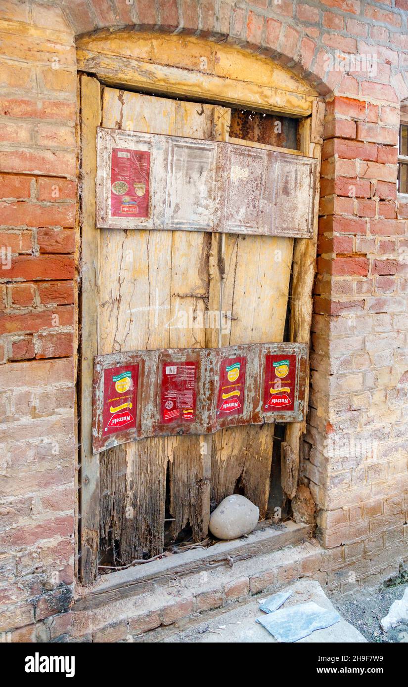 Dilapidated old wooden door in the crumbling wall of a building in Pragpur, a heritage village in Kagra district, Himachal Pradesh, India Stock Photo
