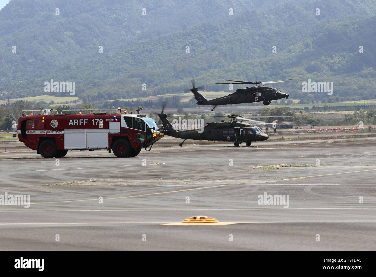 Hawaii Army National Guard (HIARNG) UH-60M Black Hawk helicopters land near a fire truck before the water salute for Sgt. Kaylen H. Hayashi, a UH-60M Black Hawk Helicopter Mechanic, with Charlie Company, 1st Battalion, 183rd Aviation Regiment, Wahiawa, Hawaii, Aug. 7, 2021. A water salute involves plumes of water shot from fire trucks over an aircraft in celebration of Hayashi’s final drill before retirement from the National Guard. (U.S. Army National Guard photo by Spc. Mariah-Alexsandra Manandic-Kapu) Stock Photo