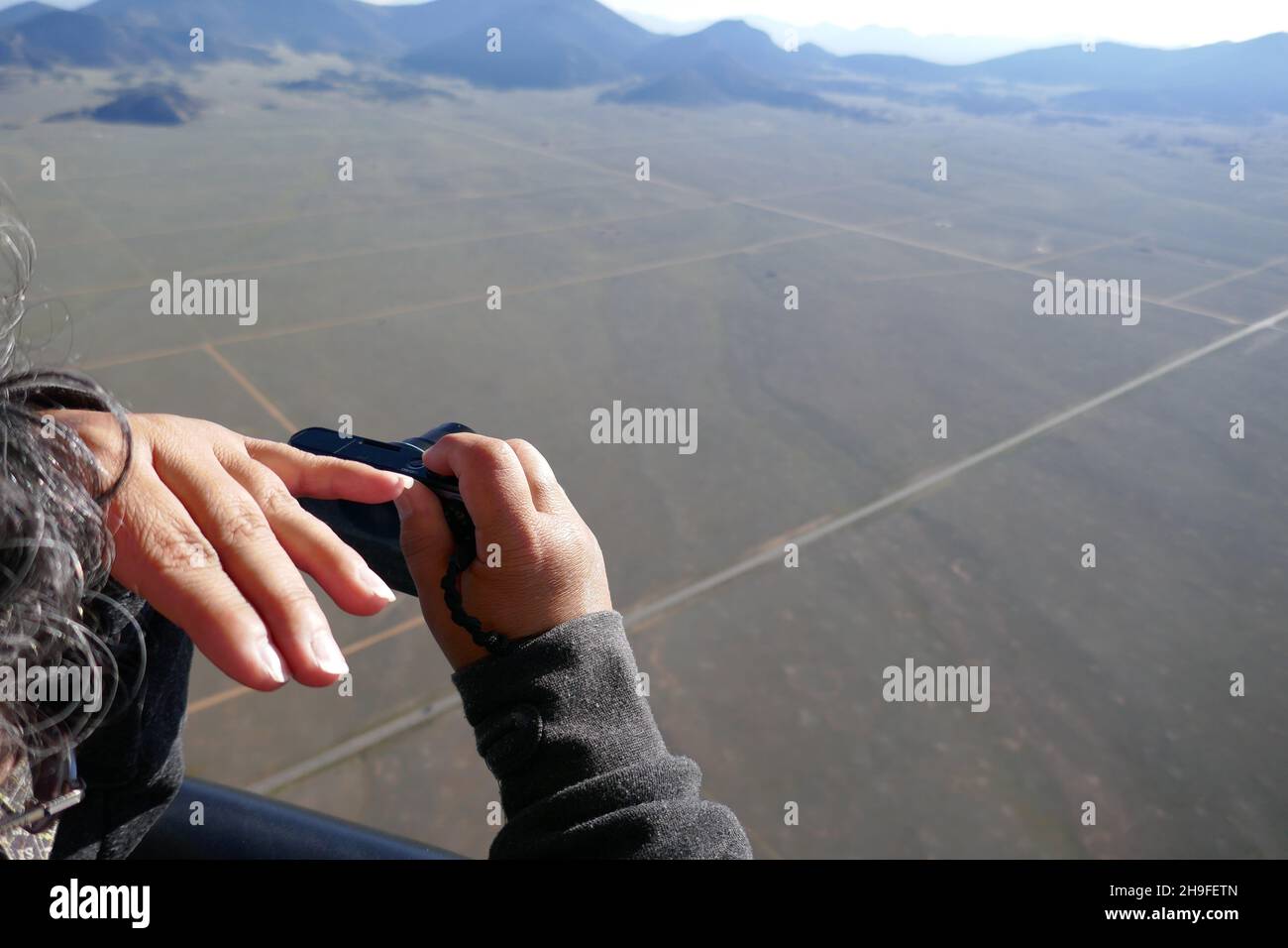 Hot air balloon passenger blocking sun with hand and taking photograph with camera Stock Photo