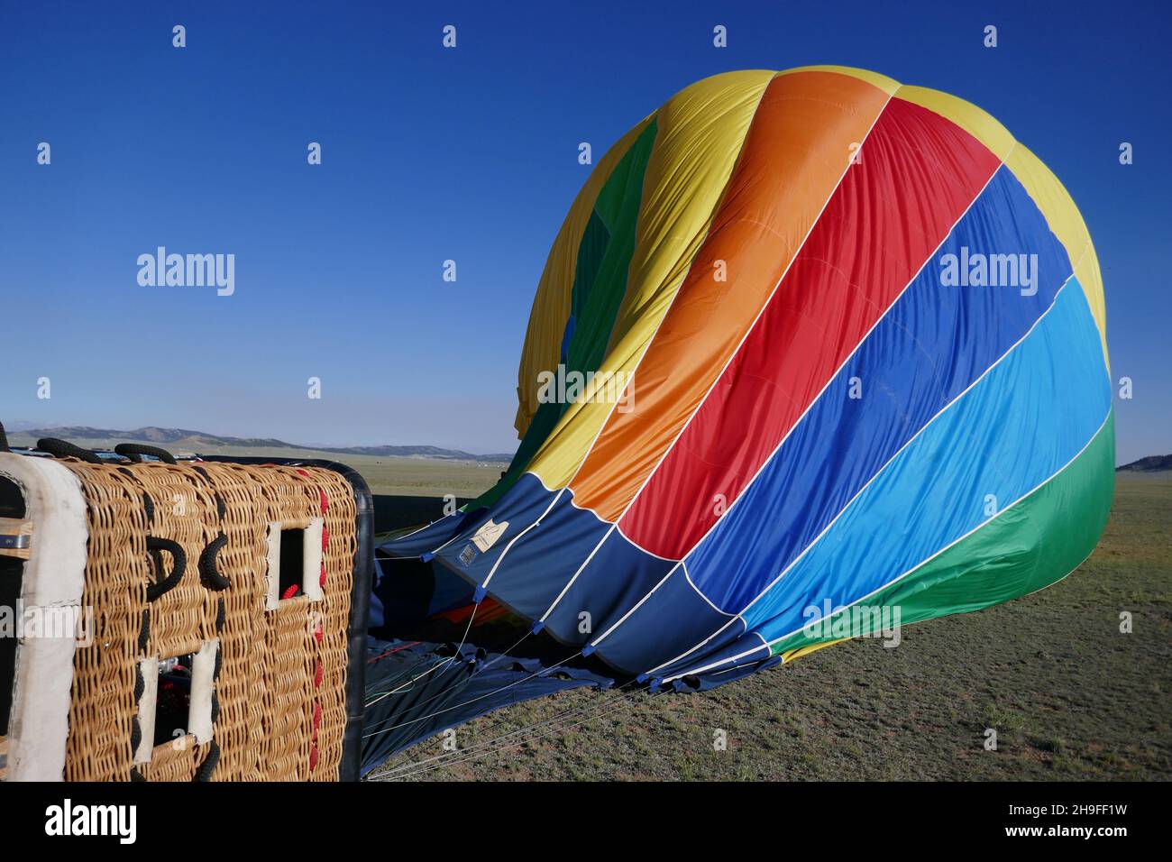Colorful hot air balloon with passenger basket attached deflating Stock