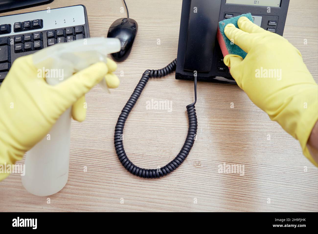 Cleaning the office, a janitor in yellow gloves wipes telephone and ...