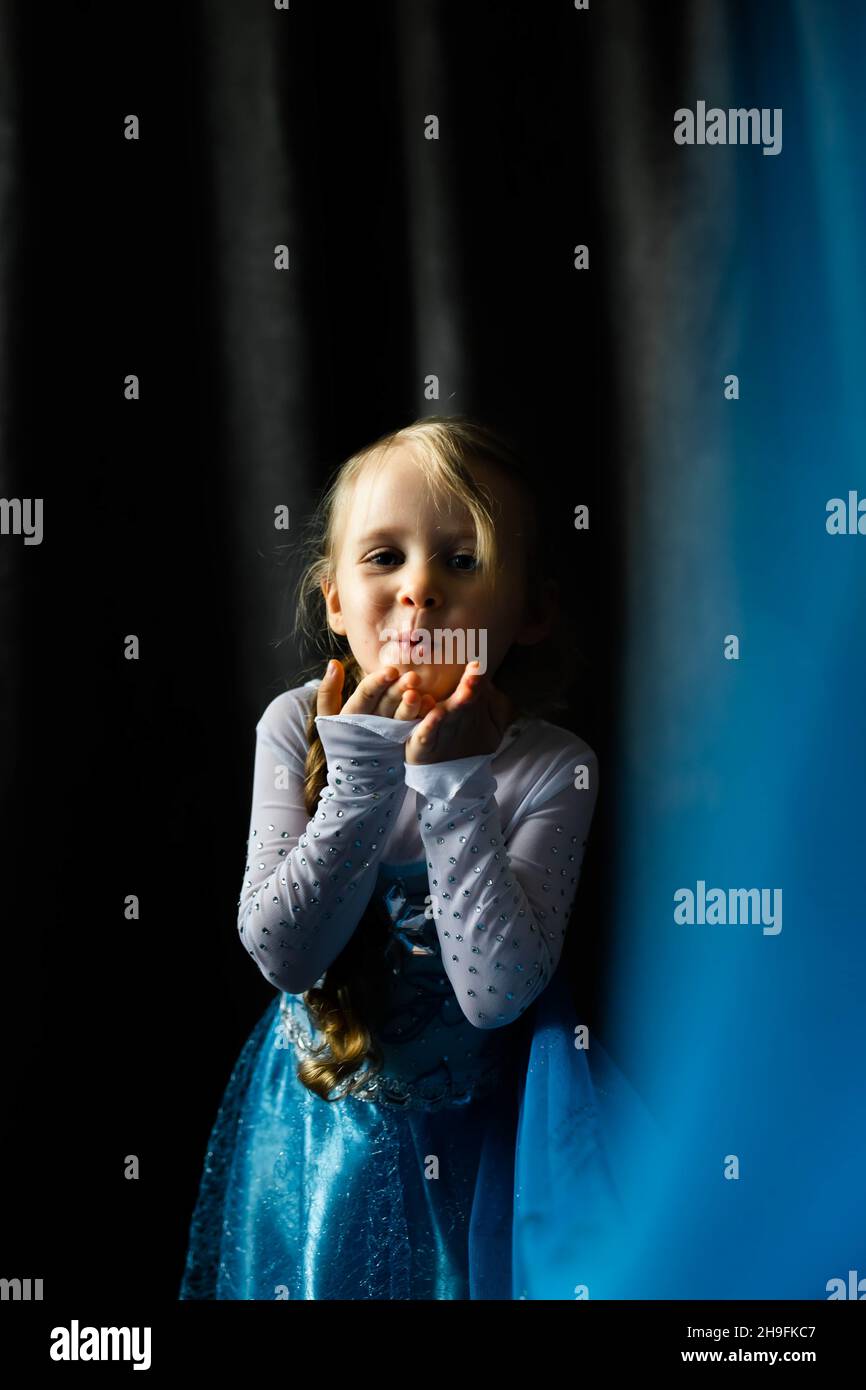 A portrait of a little girl sending an air kiss on a dark blue background. Front view. Stock Photo