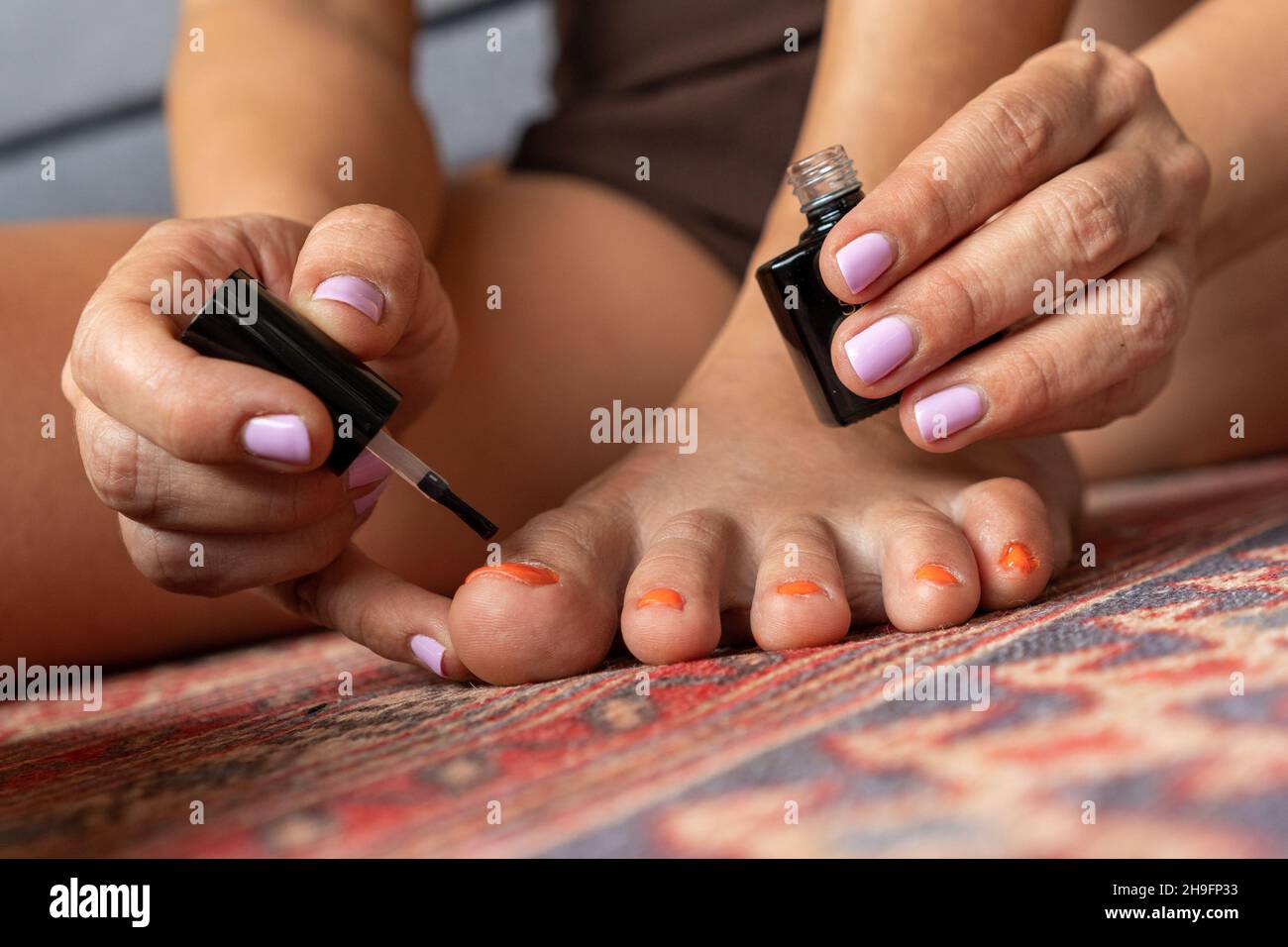 Woman with ugly feet painting her toenails with orange nail polish Stock Photo