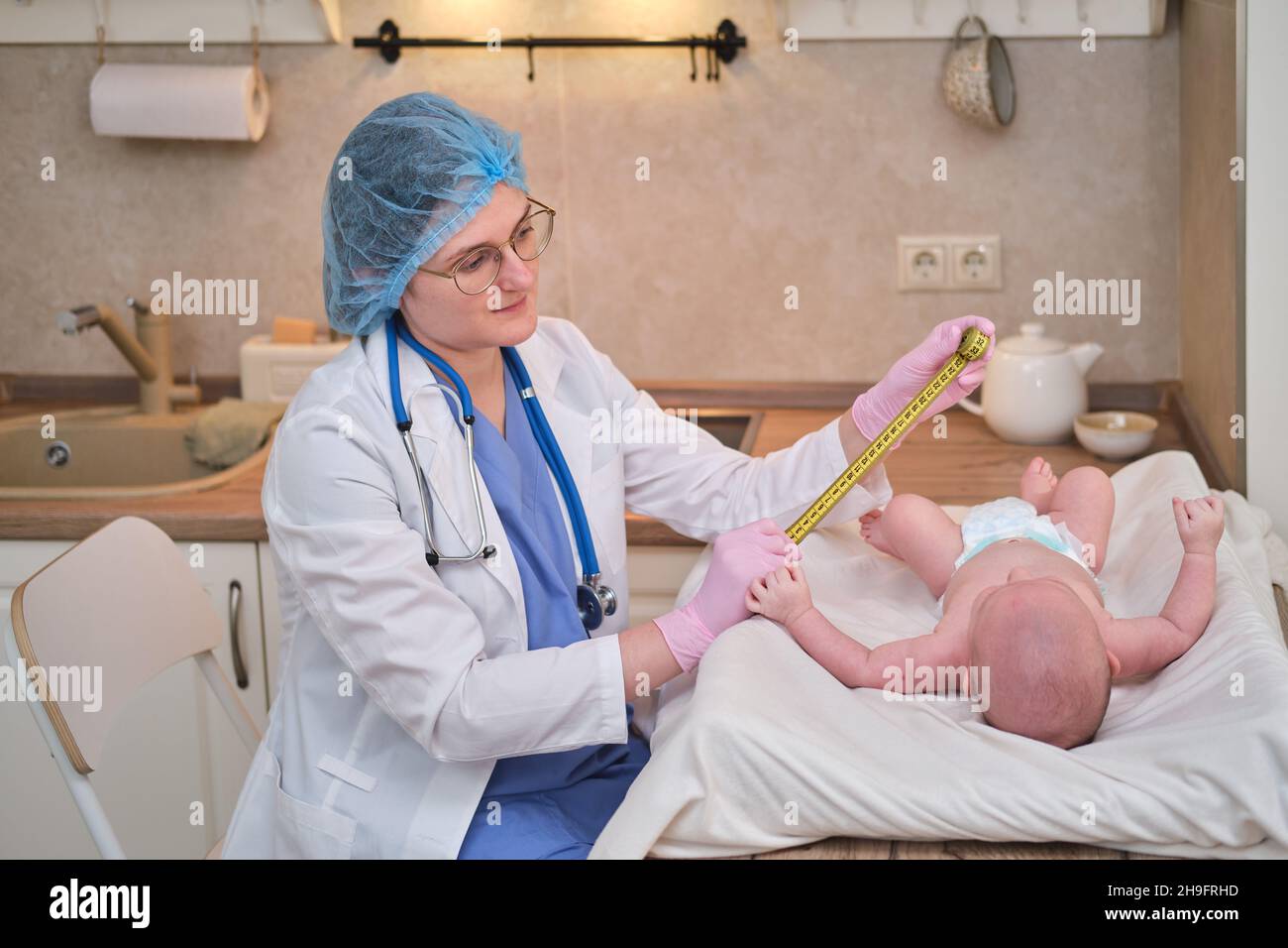 Doctor measures the growth of a newborn baby. A nurse in uniform checks the girth of the child head and abdomen Stock Photo