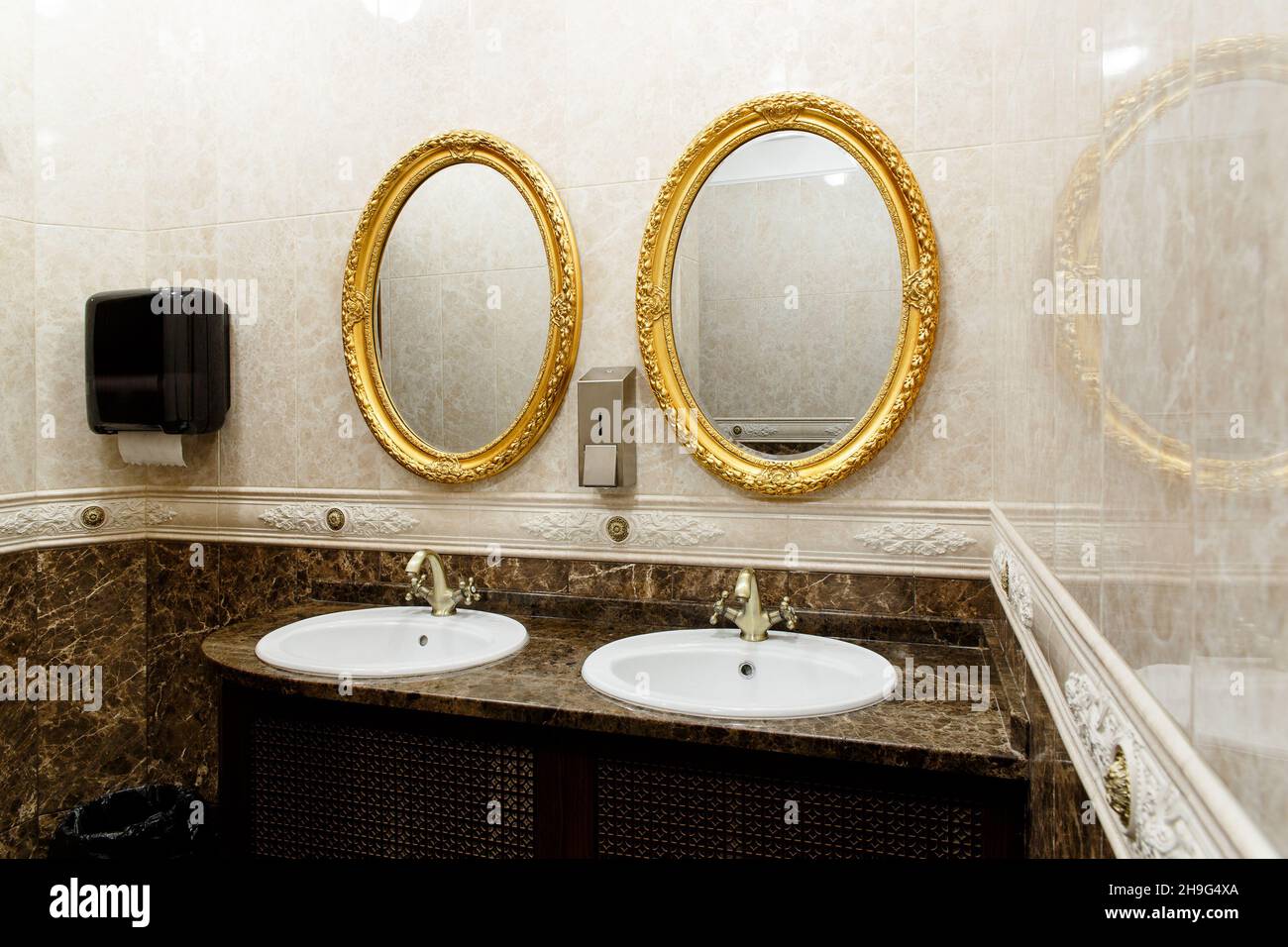 Two modern ceramic washbasins with mirrors in the restroom of the restaurant. Ceramic sink with bronze mixer in contemporary toilet . Interior of Euro Stock Photo