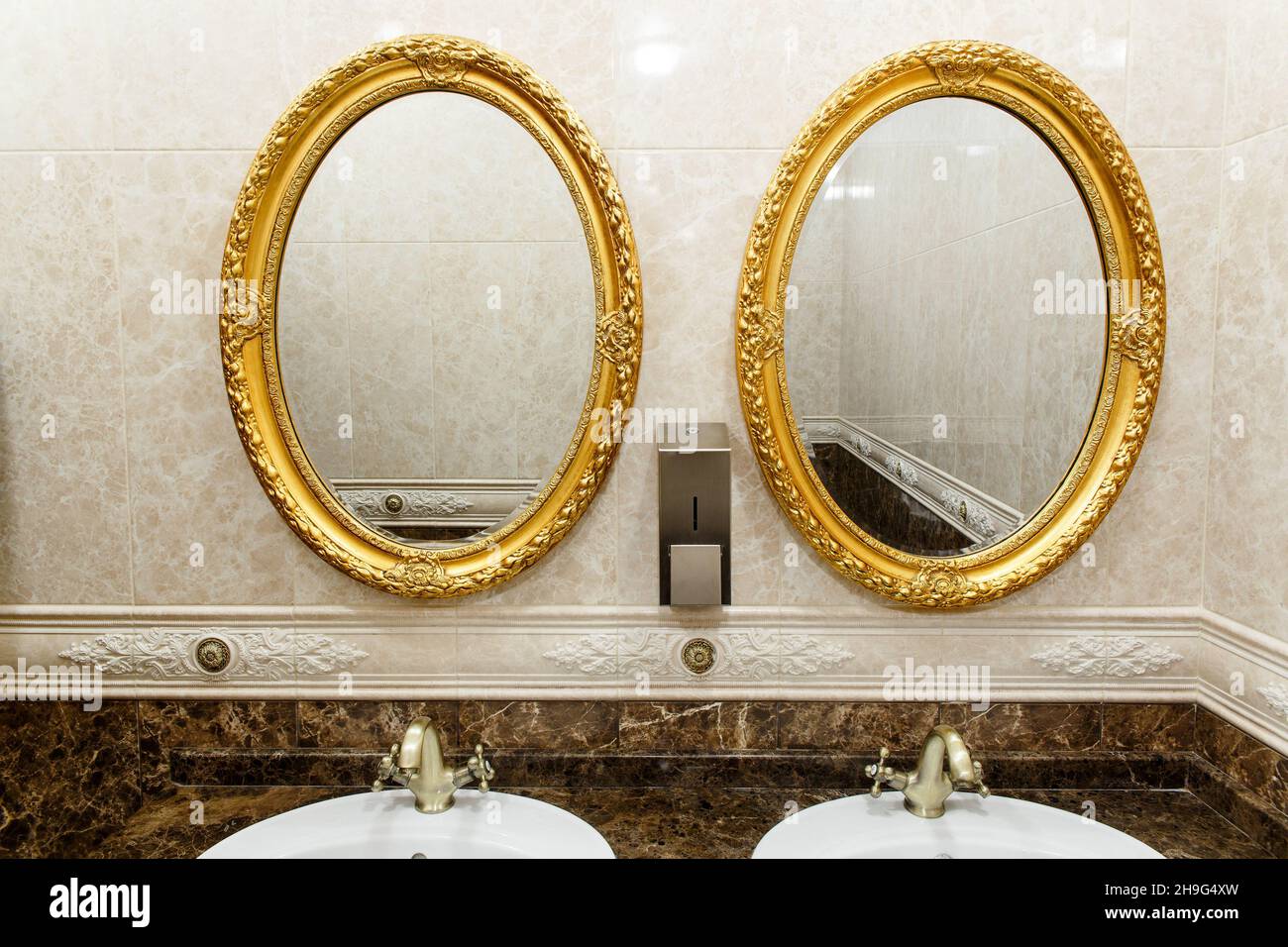 Two modern ceramic washbasins with mirrors in the restroom of the restaurant. Ceramic sink with bronze mixer in contemporary toilet . Interior of Euro Stock Photo