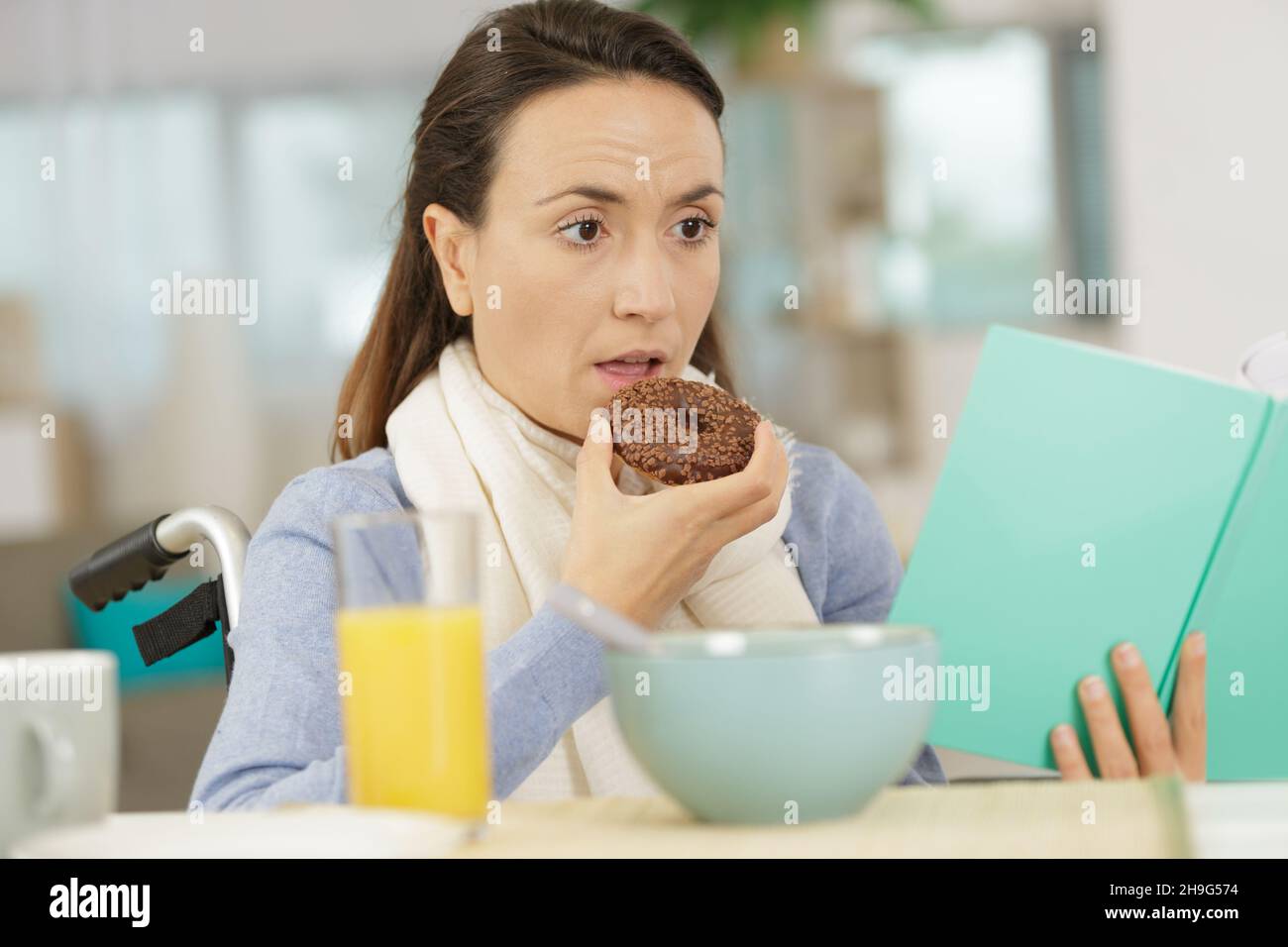 young disabled woman eating a donut while reading a book Stock Photo