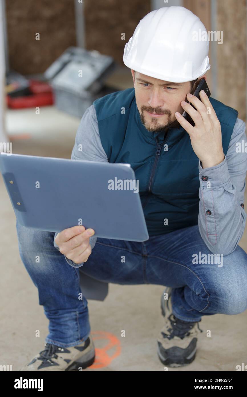 constructor reading something from clipboard notes and talking on telephone Stock Photo