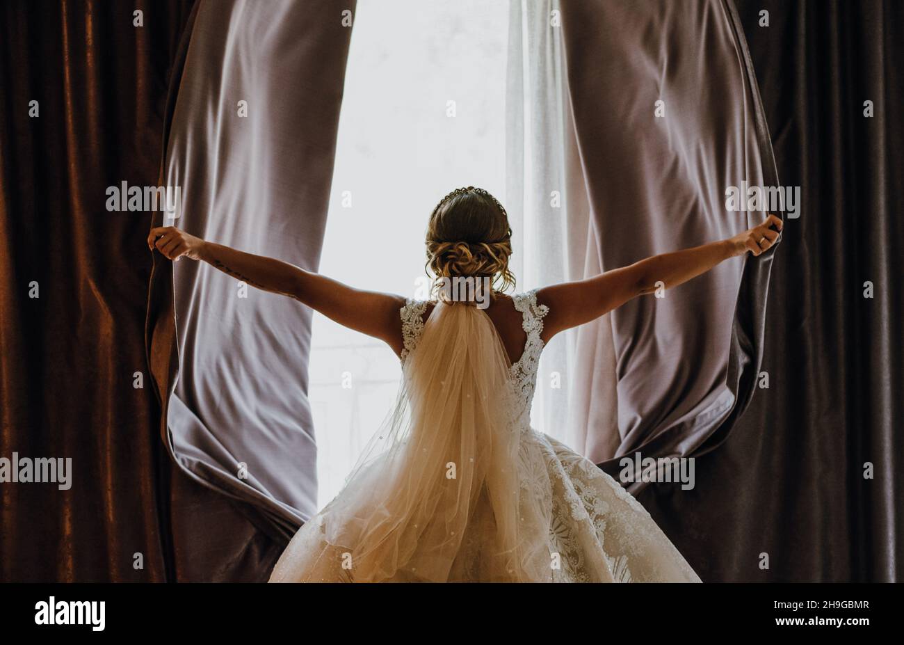 Closeup shot of a bride from the back opening curtains widely