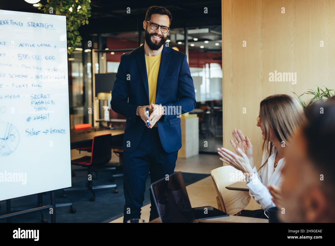 Successful businessman receiving an applause from his team in a modern workspace. Happy young businessman smiling during his presentation to his colle Stock Photo