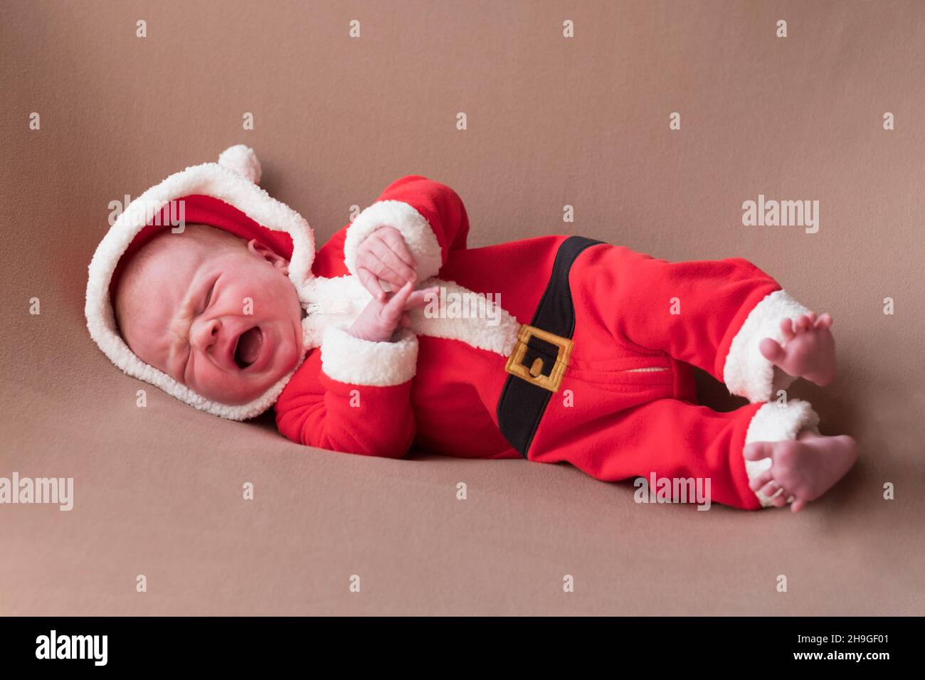 Newborn girl dressed in santa claus costume looking at camera with confused face. Stock Photo