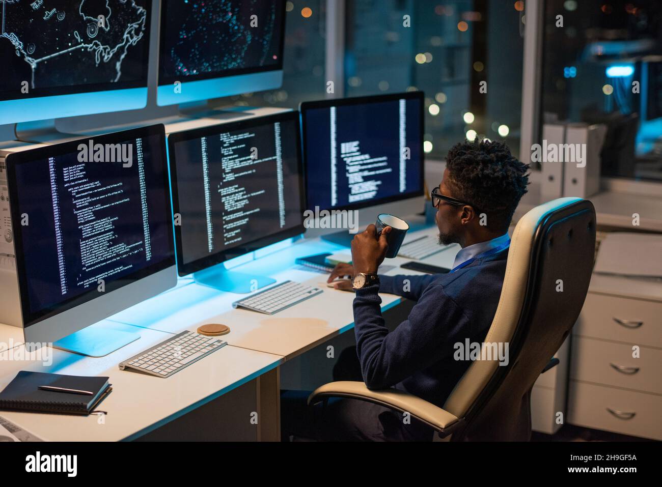 Young African programmer with drink looking at coded data on computer screen while working in office Stock Photo