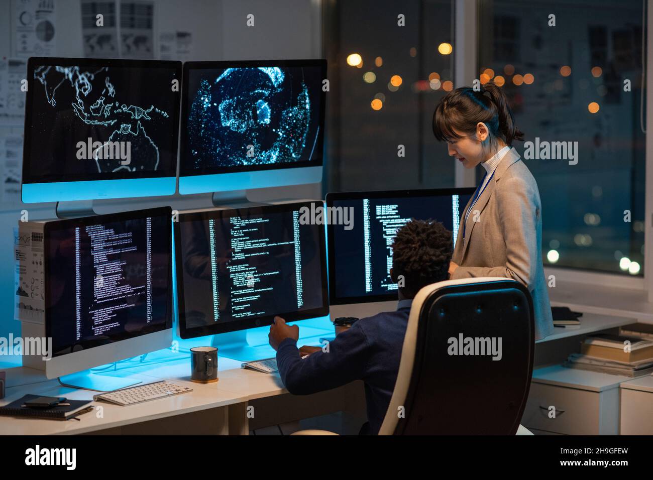 Two intercultural programmers consulting about working points while decoding data on computer screen in office Stock Photo