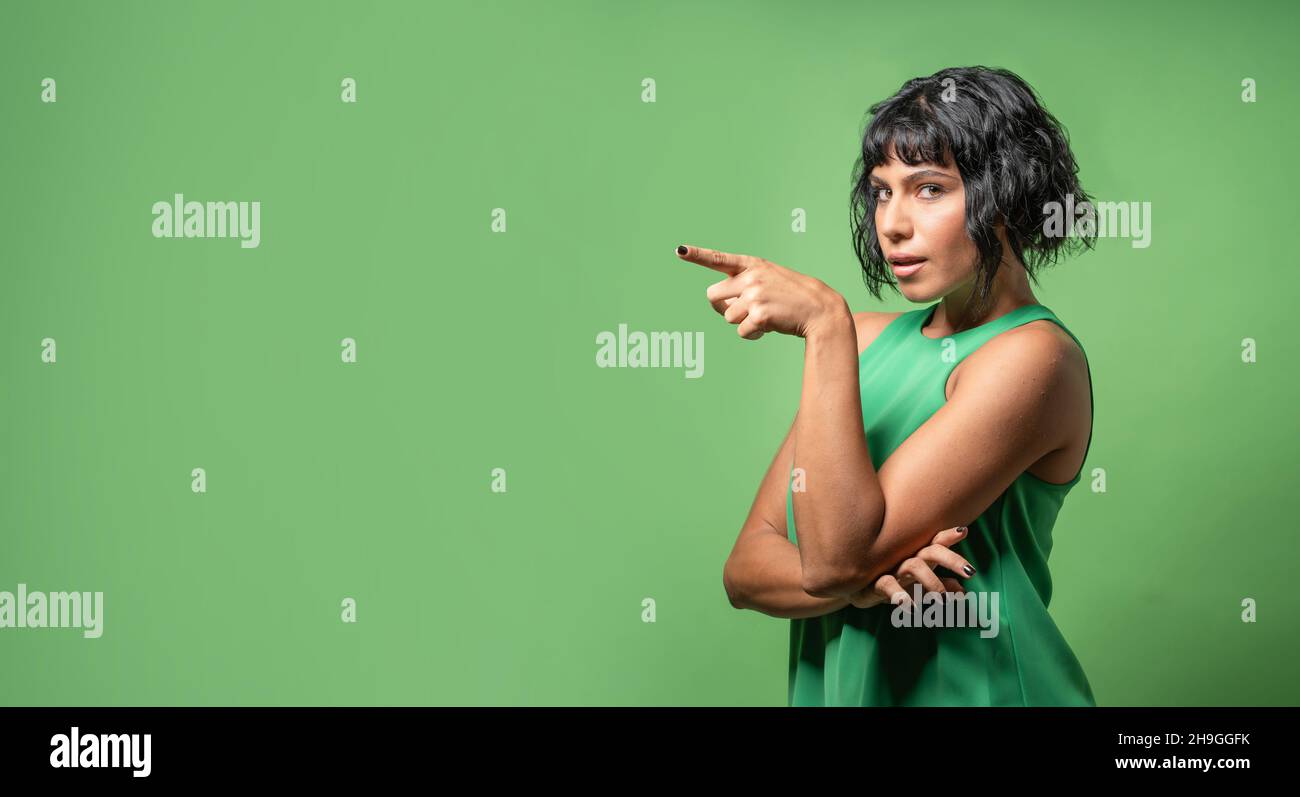 Portrait of a young brunette woman pointing on an empty space - girl isolated on a green colored  background Stock Photo