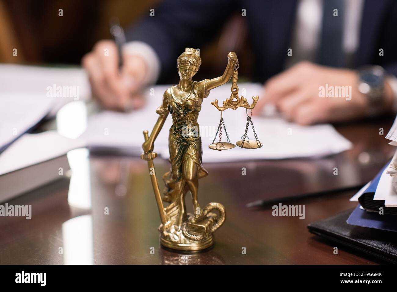 Statue of Lady Justice with her eyes bound holding scales against hands of contemporary lawyer signing papers Stock Photo