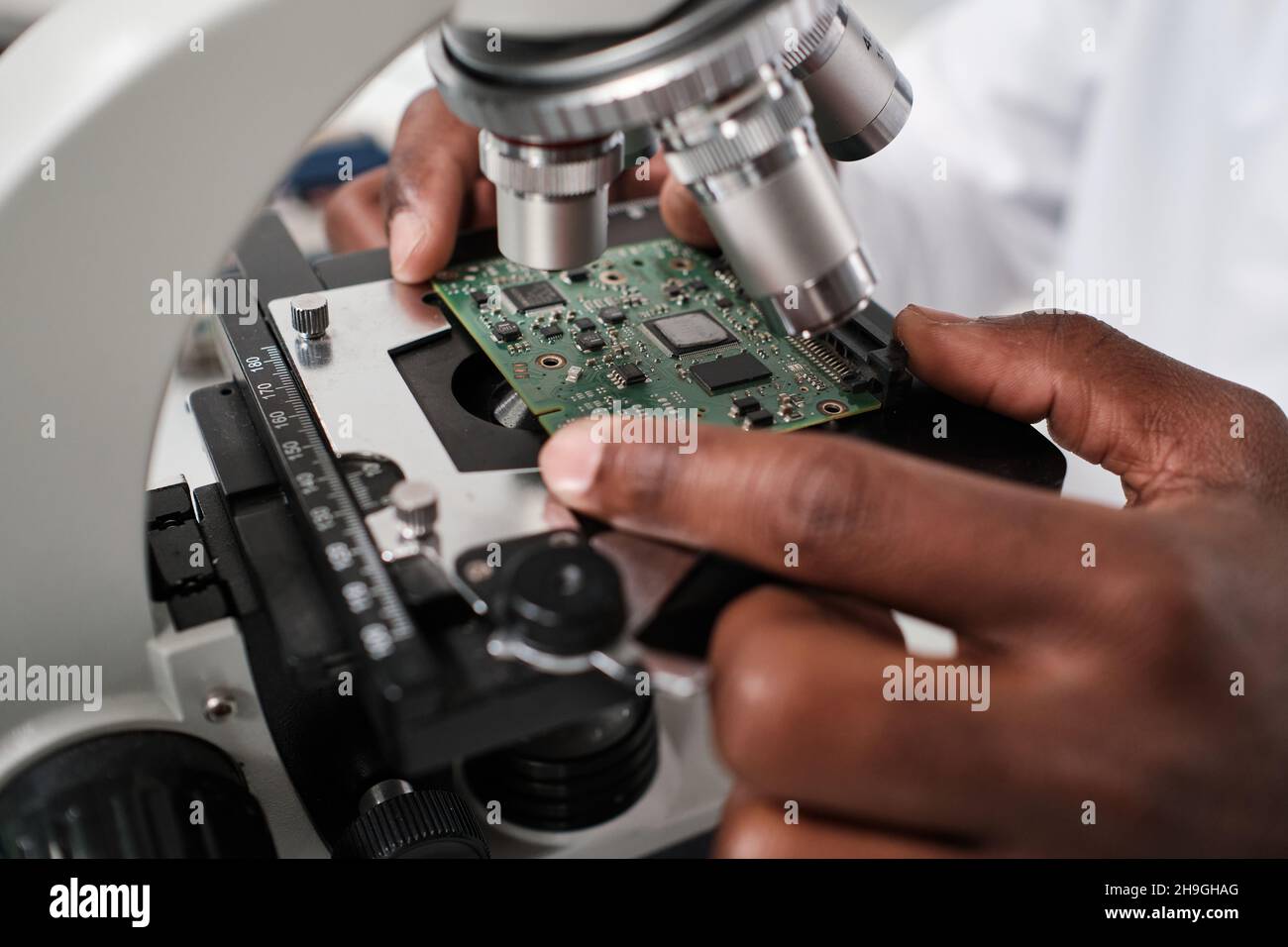 Part of hand of contemporary researcher putting circuit board in microscope before studying its characteristics Stock Photo