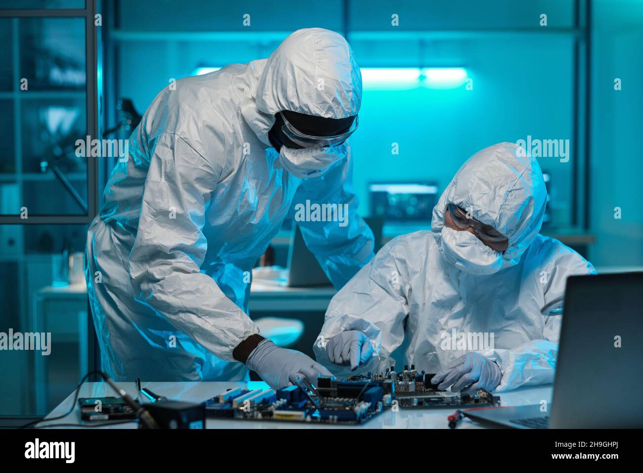 Electronics Rework Lab Two contemporary lab workers in protective coveralls consulting about ...