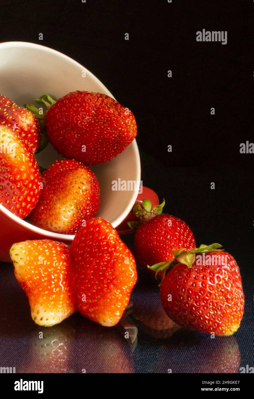 The Strawberries in cup on black background and table with reflection. Red ripe berries by summer Stock Photo