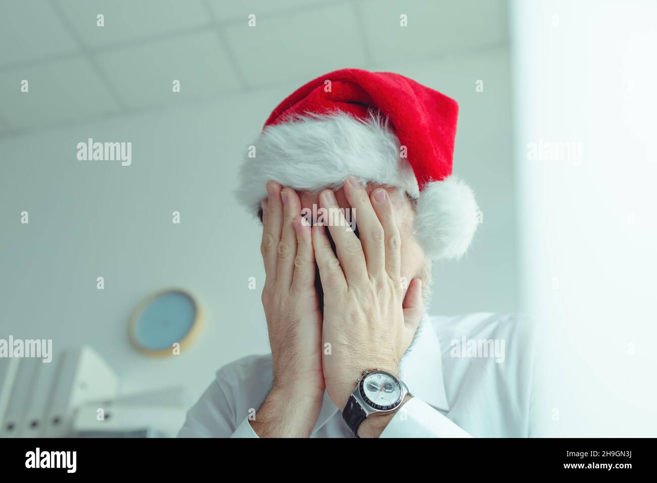 Sad businessman with Santa Claus hat suffering from Christmas holiday season depression in office, selective focus Stock Photo