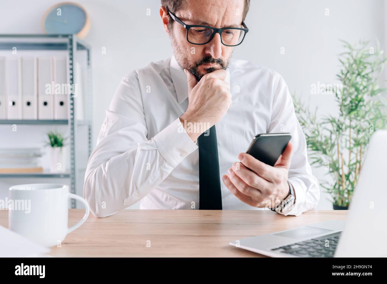 Upsetting text message notification, businessman with mobile smart phone in office receiving bad sms with disturbing content, selective focus Stock Photo