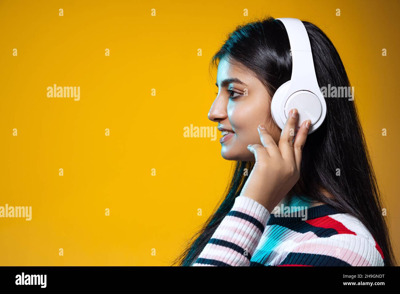 Profile view of young girl with long black hair listening to music in ...