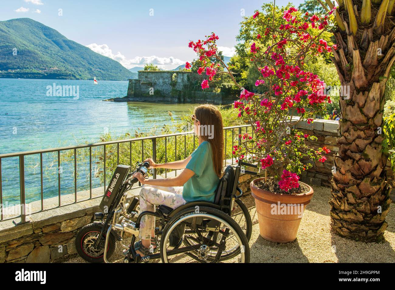Young woman in wheelchair enjoying view on lakeside and mountains - Junge Rollstuhlfahrerin geniesst die Aussicht am Seeufer auf See und Berge Stock Photo