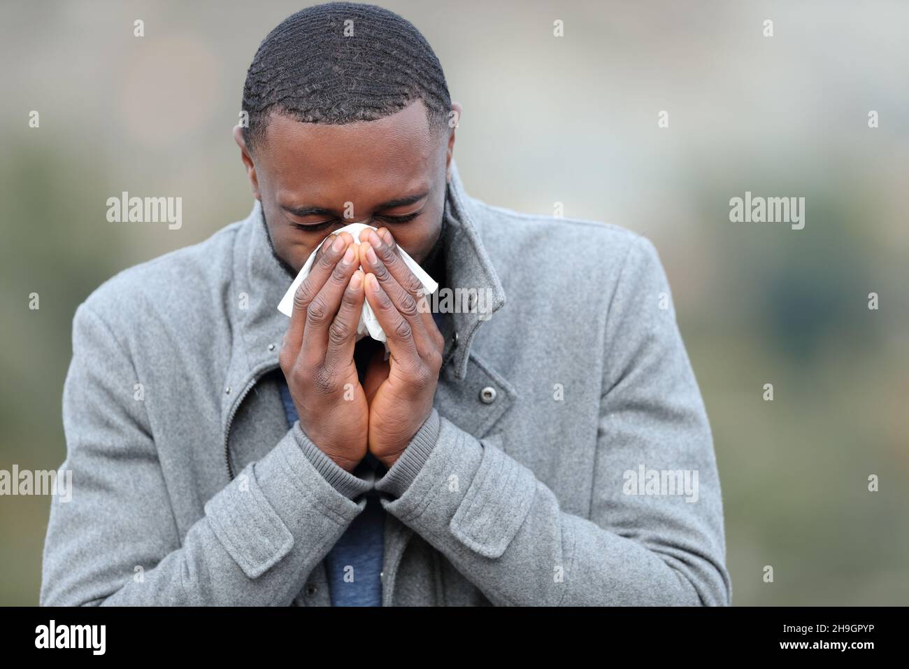 Ill man with black skin blowing on tissue outddors in winter Stock Photo