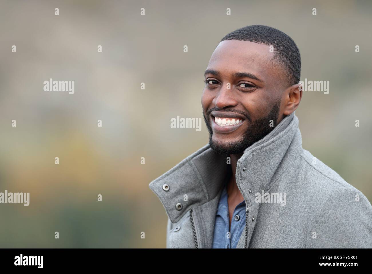 Happy man with black skin looking at you standing outdoors in winter Stock Photo