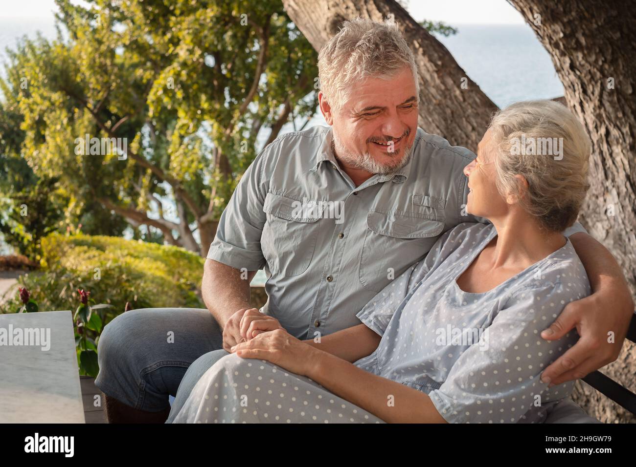 Elderly couple on vacation in a restaurant overlooking the sea. A man and a woman look at each other while sitting at a table Stock Photo