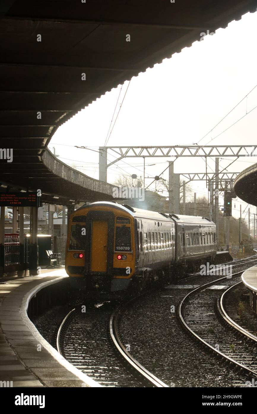 Northern express sprinter diesel-multiple unit train leaving Carnforth station, platform 1, on 6th December 2021, rain shower and glint from sunlight. Stock Photo