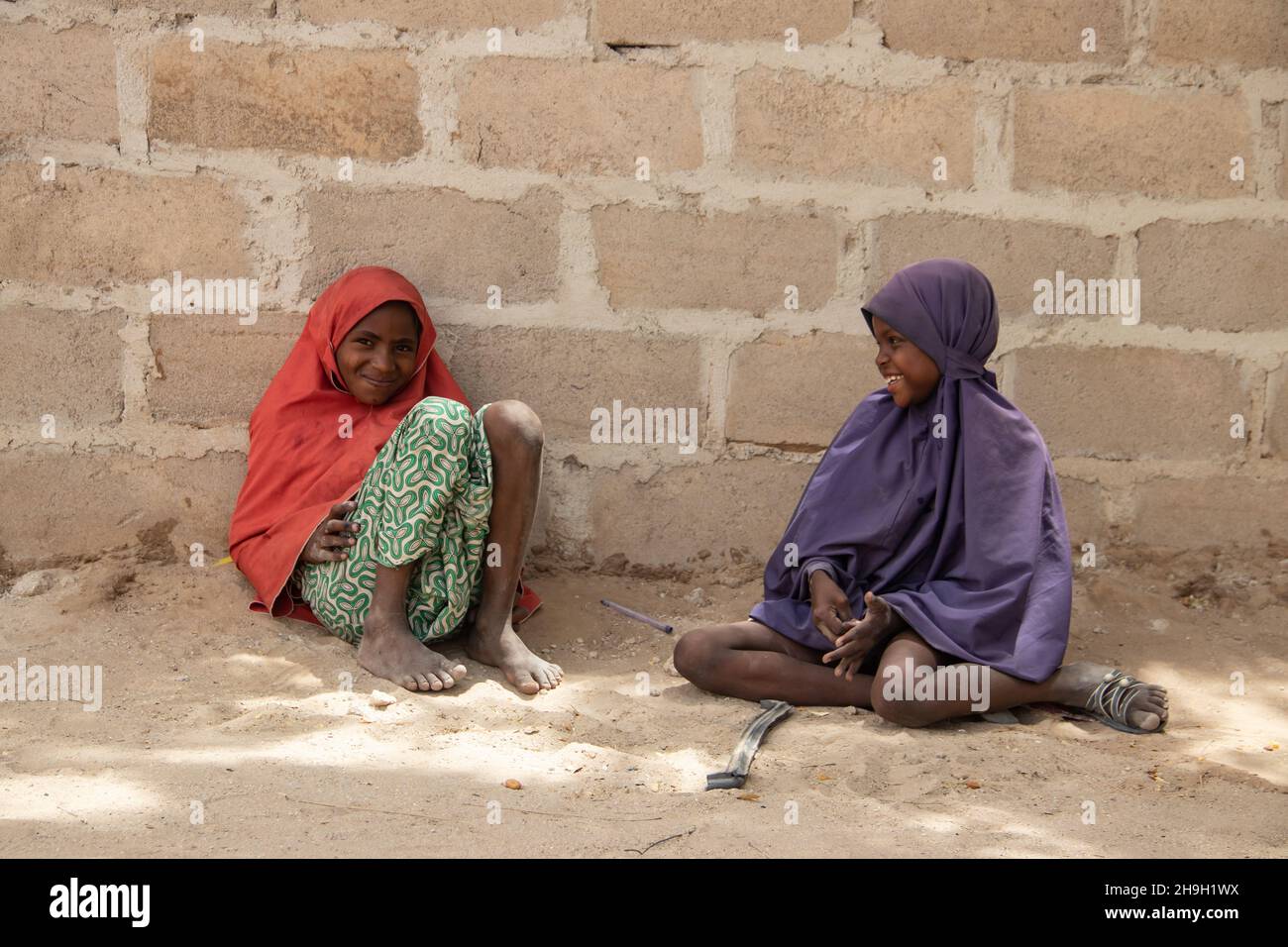 Two sisters dressed in traditional colorful wardrobe seating at the ground, Nigeria, Maiduguri Stock Photo