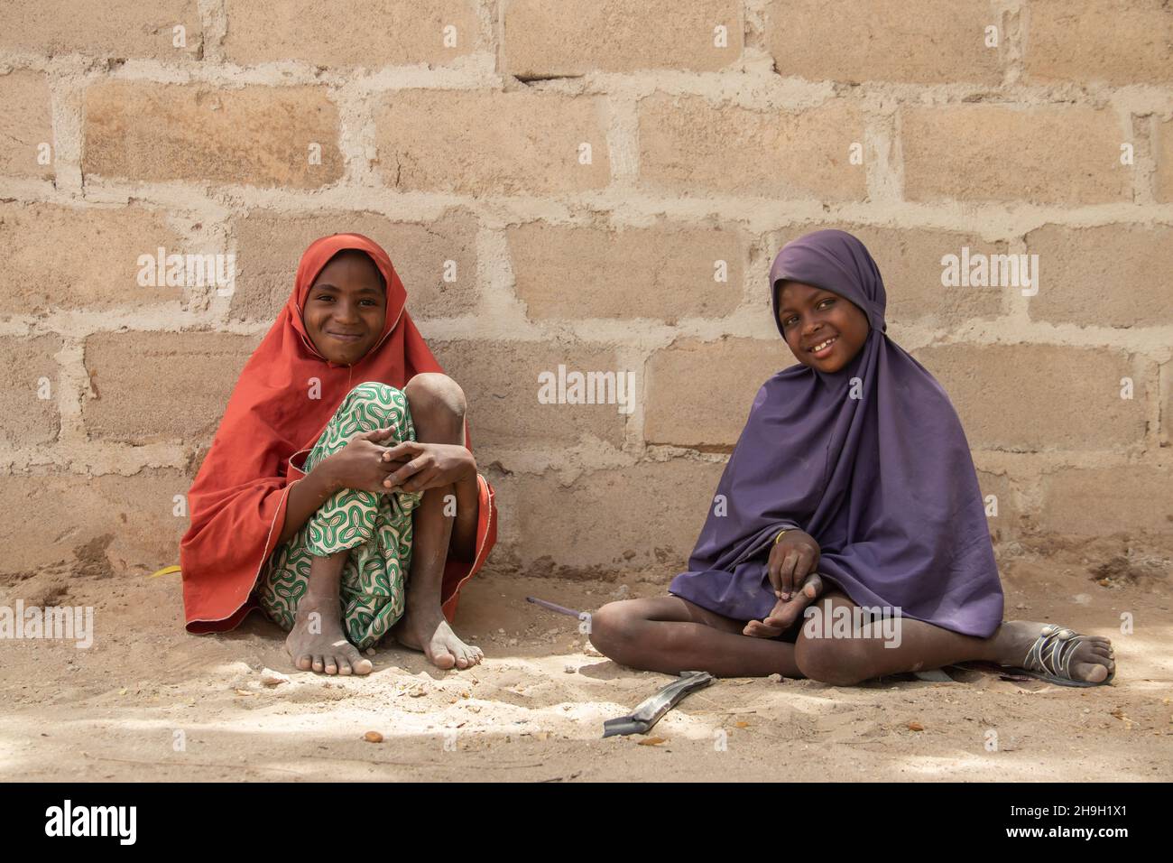 Two sisters dressed in traditional colorful wardrobe seating at the ground, Nigeria, Maiduguri Stock Photo