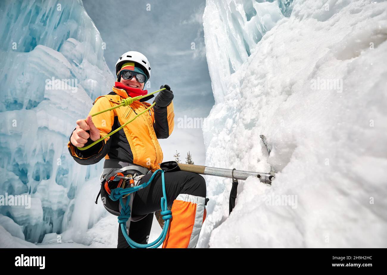 Portrait of woman climber near frozen waterfall with ice axe and rope knot in orange jacket in the mountains Stock Photo