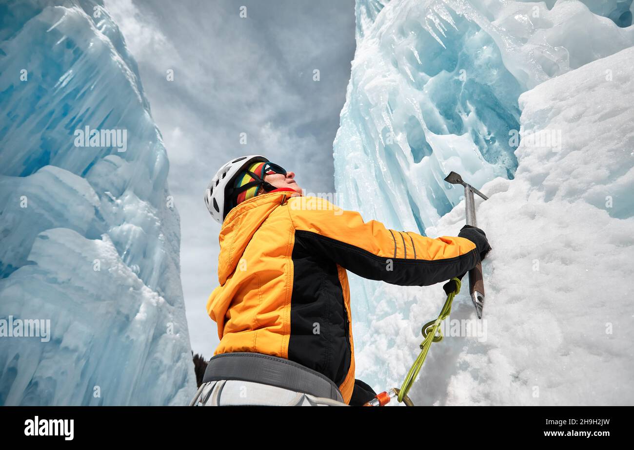 Woman is climbing frozen waterfall with ice axe in orange jacket in the mountains Stock Photo