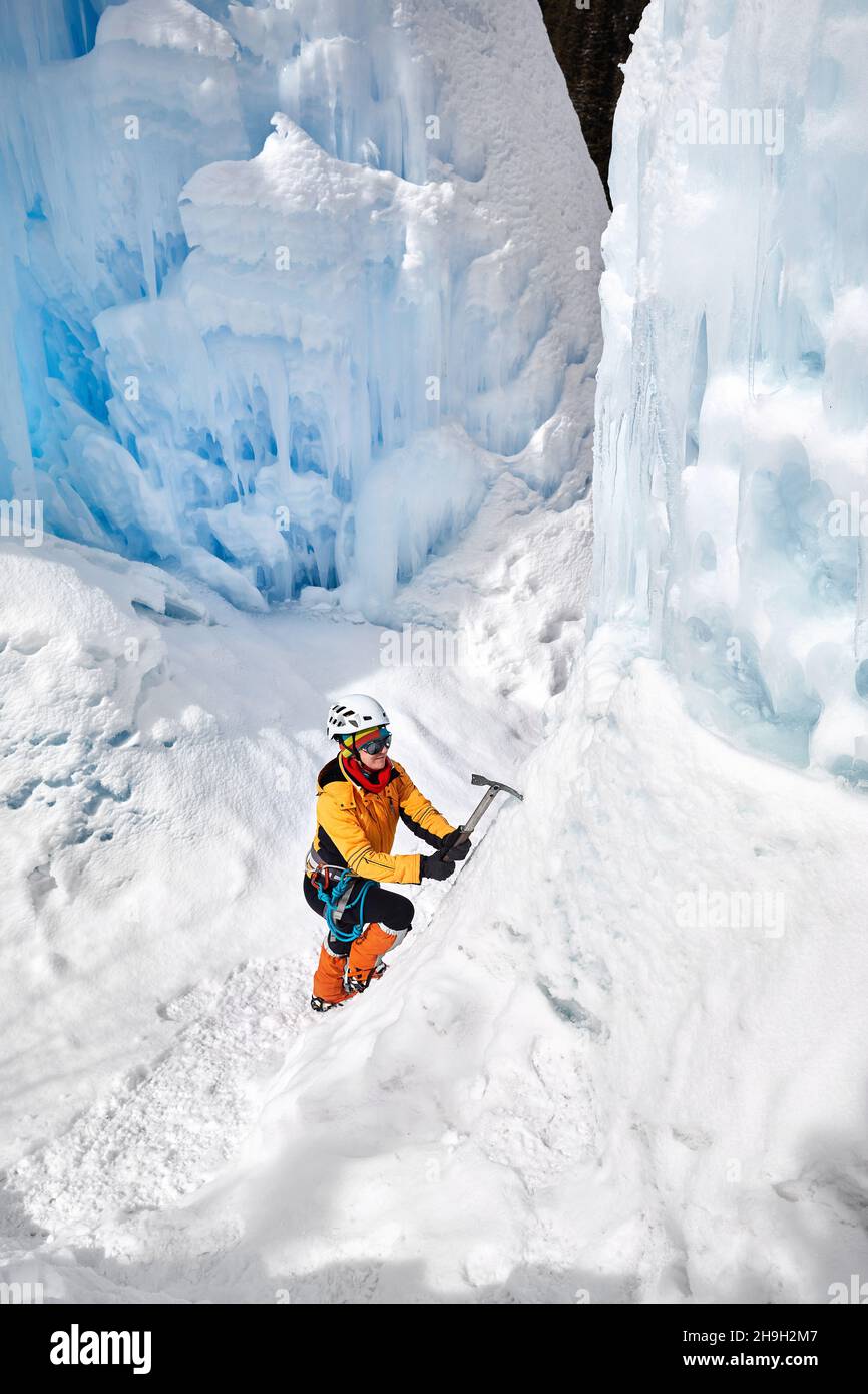 Woman climber in orange jacket with ice axe near frozen waterfall in the mountains in Almaty, Kazakhstan Stock Photo