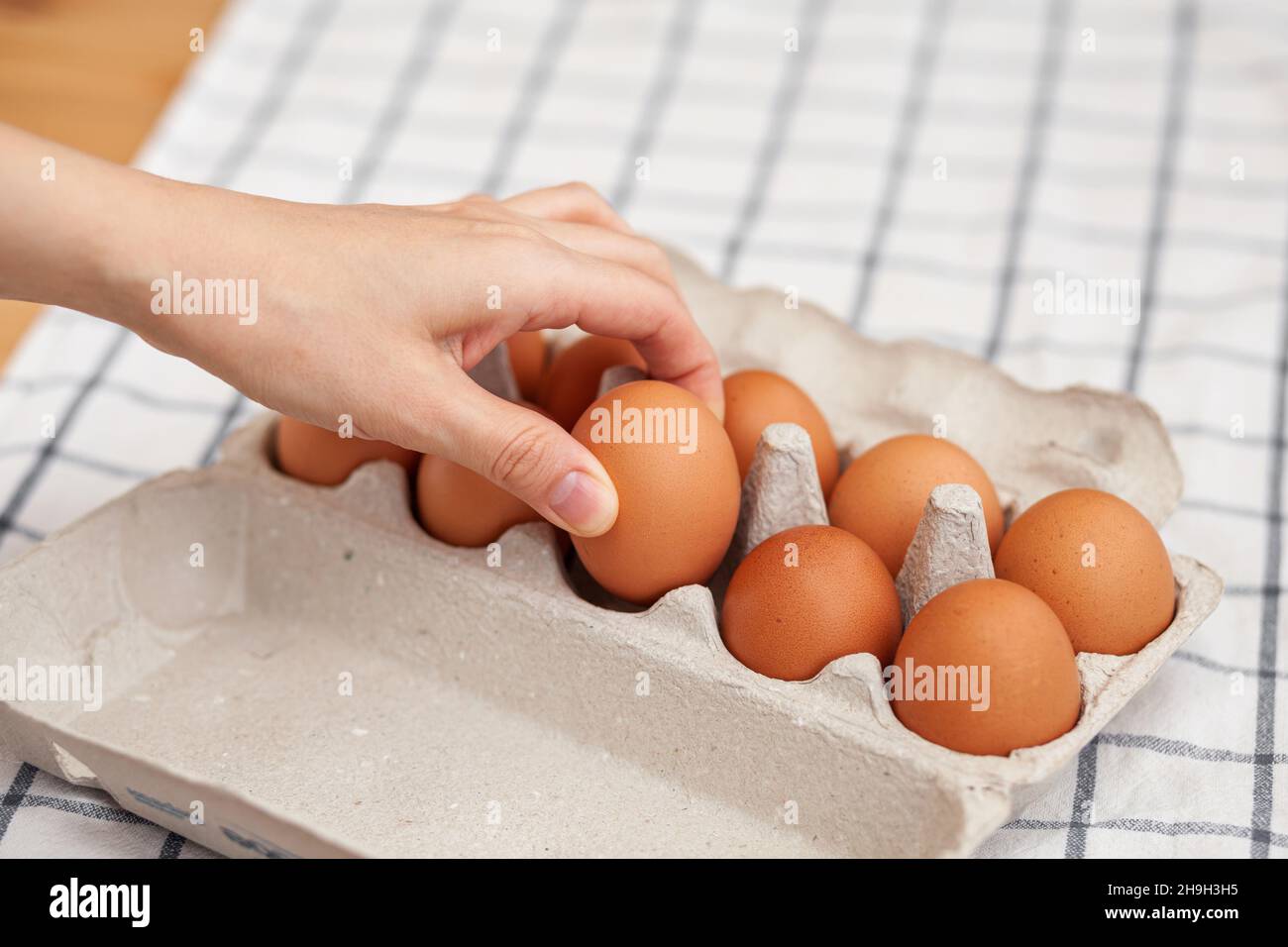 Chicken brown eggs are in a cardboard box bought at a grocery store. Healthy breakfast. A tray for carrying and storing fragile eggs. Woman takes one Stock Photo