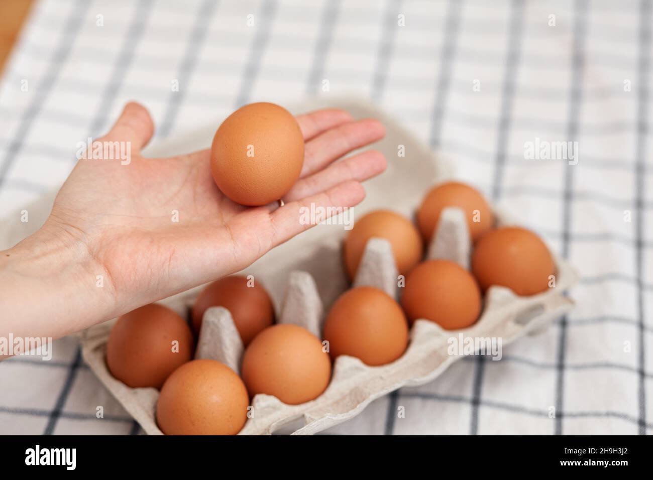 Chicken brown eggs are in a cardboard box bought at a grocery store. Healthy breakfast. A tray for carrying and storing fragile eggs. Woman takes one Stock Photo
