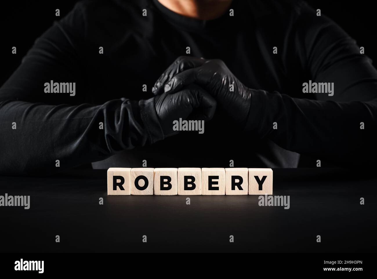Theft, crime, robbery or burglary concept. The word robbery written on wooden blocks with a thief with black gloves background. Stock Photo