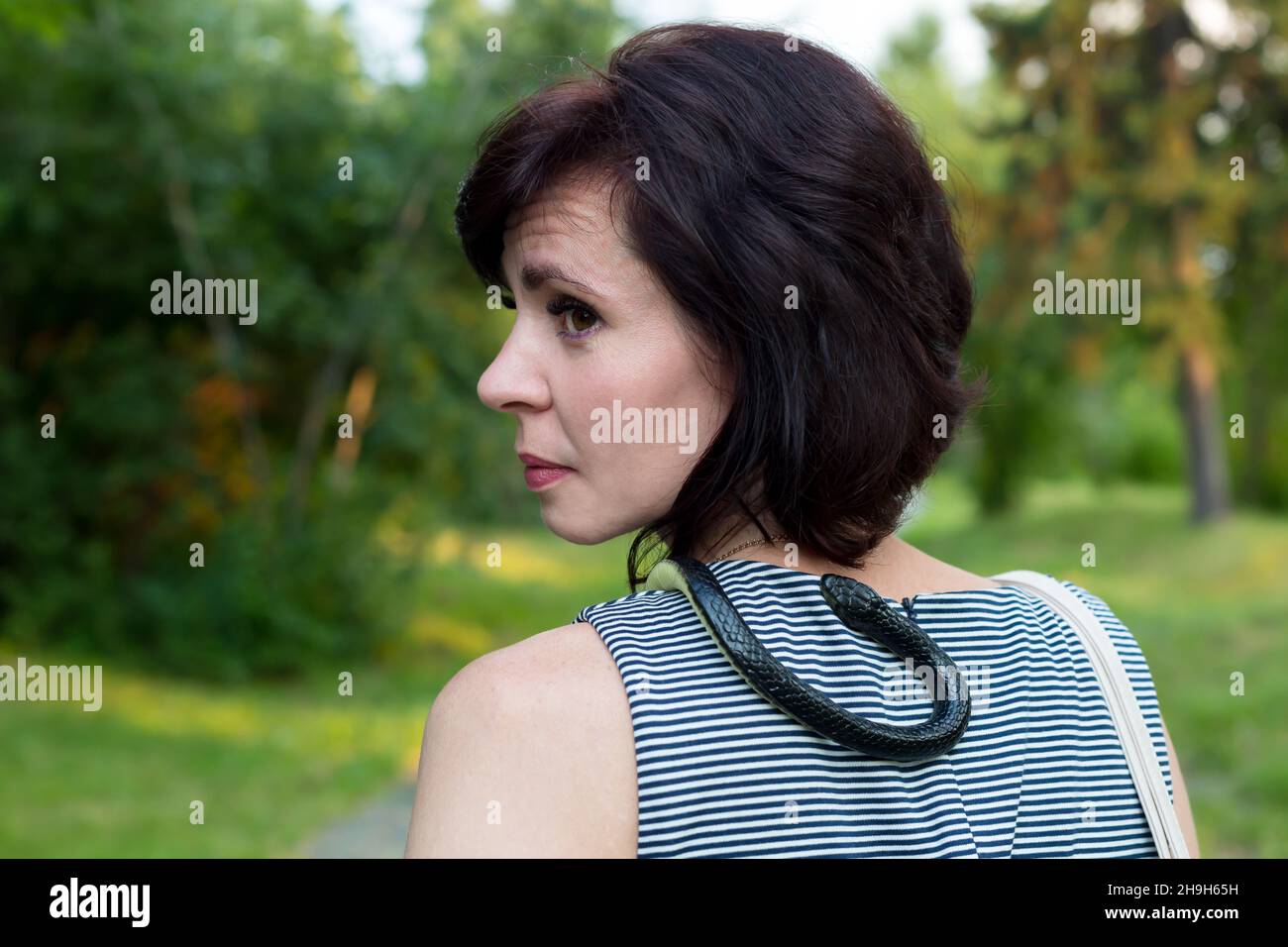 A woman with a live snake around her neck walks through the park. Stock Photo