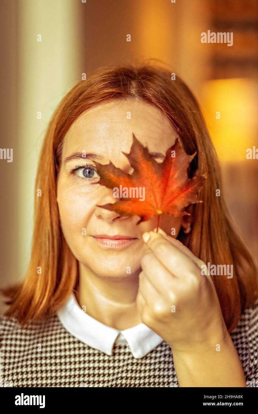 Portrait of a young woman covering one eye with an autumn fallen maple ...