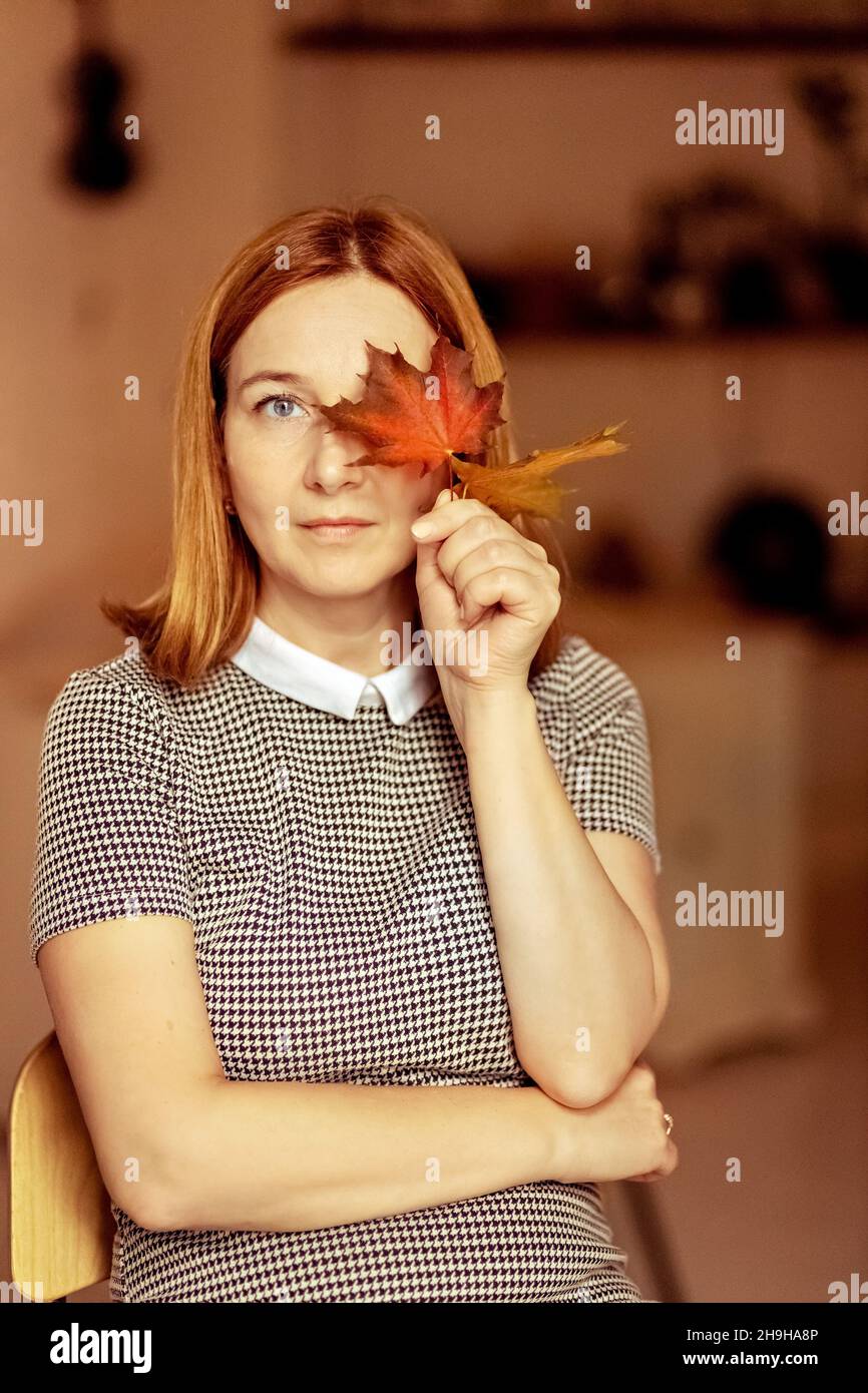 Portrait of a young woman covering one eye with an autumn fallen maple ...