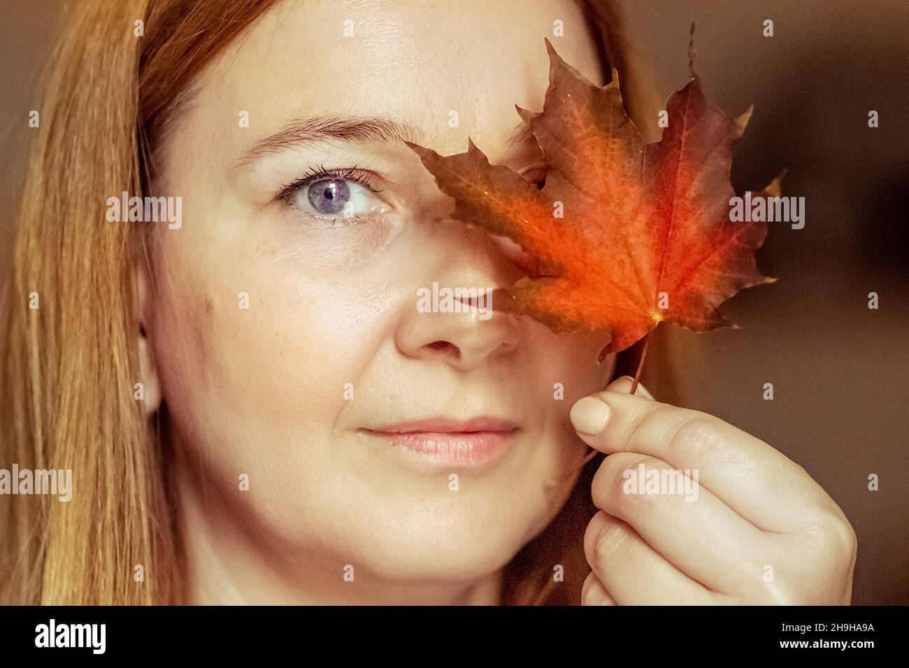 Portrait of a young woman covering one eye with an autumn fallen maple ...