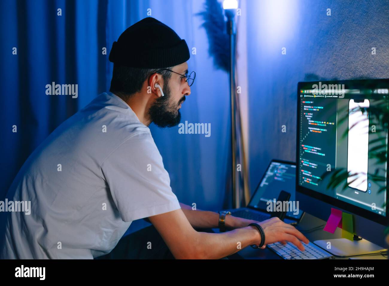 Young man mobile developer writes program code on a computer, programmer work in home office. Stock Photo