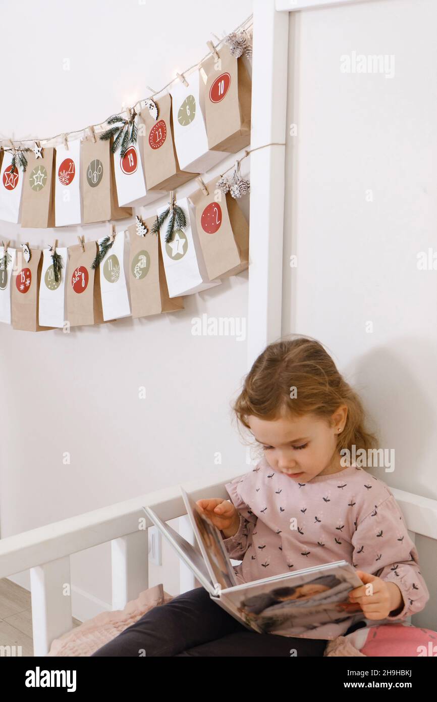 Mather with toddler child reading book or photo album on Christmas eve near eco advent calendar in kids room on the bed. Night story for girl with Stock Photo